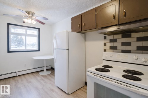 Kitchen with white appliances, decorative backsplash, light wood-style flooring, a textured ceiling, and a ceiling fan - 3917/3919 54 Street, Wetaskiwin, AB - Indoor Photo Showing Kitchen