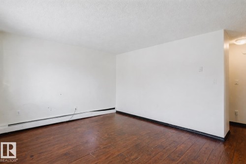 Empty room with a baseboard radiator, dark wood-style floors, and a textured ceiling - 3917/3919 54 Street, Wetaskiwin, AB - Indoor Photo Showing Other Room