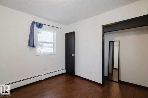Unfurnished bedroom with a baseboard heating unit, a textured ceiling, and dark wood-style floors - 3917/3919 54 Street, Wetaskiwin, AB - Indoor Photo Showing Other Room