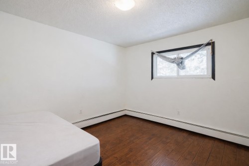 Unfurnished bedroom featuring a textured ceiling, dark wood-type flooring, and baseboard heating - 3917/3919 54 Street, Wetaskiwin, AB - Indoor Photo Showing Other Room