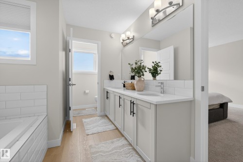 Ensuite bathroom with tasteful backsplash, double vanity, light wood-style floors, and a bath - 19286 22A Avenue, Edmonton, AB 