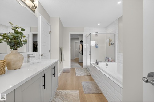 Full bathroom featuring a walk in closet, a shower stall, light wood-type flooring, vanity, and a garden tub - 19286 22A Avenue, Edmonton, AB 