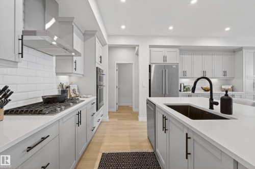 Kitchen with backsplash, light wood-style floors, stainless steel appliances, light stone counters, and recessed lighting - 19286 22A Avenue, Edmonton, AB 