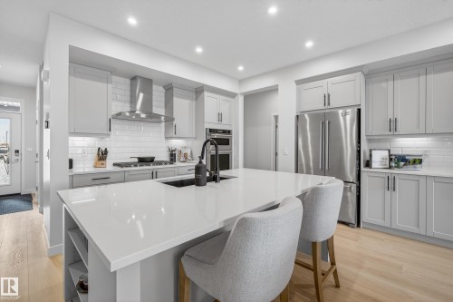 Kitchen with light wood finished floors, stainless steel appliances, a kitchen island with sink, decorative backsplash, and recessed lighting - 19286 22A Avenue, Edmonton, AB 
