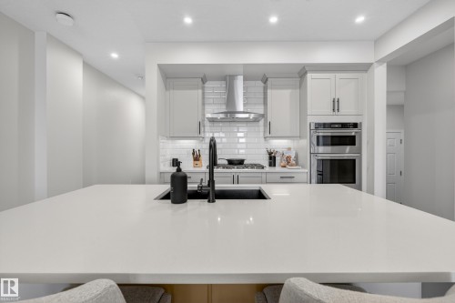 Kitchen with light stone countertops, stainless steel double oven, white cabinets, recessed lighting, and extractor fan - 19286 22A Avenue, Edmonton, AB 