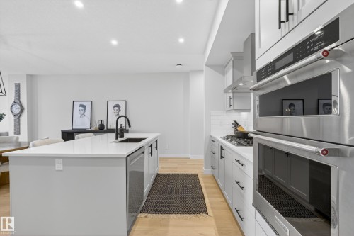 Kitchen with stainless steel appliances, light wood-style flooring, a center island with sink, white cabinetry, and recessed lighting - 19286 22A Avenue, Edmonton, AB 