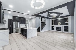 Kitchen with dark cabinetry, light stone counters, built in features, a glass covered fireplace, and freestanding refrigerator - 