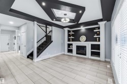 Unfurnished living room with built in features, a glass covered fireplace, a tray ceiling, and stairway - 