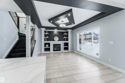 Unfurnished living room with a glass covered fireplace, built in features, a tray ceiling, and stairs - 