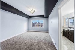 Unfurnished bedroom featuring a raised ceiling, light carpet, a textured ceiling, and ensuite bath - 