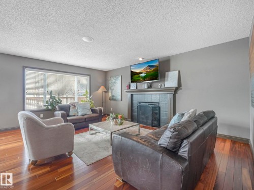 Living room with hardwood / wood-style floors, a tile fireplace, and a textured ceiling - 960 Summerside Link, Edmonton, AB - Indoor Photo Showing Living Room With Fireplace