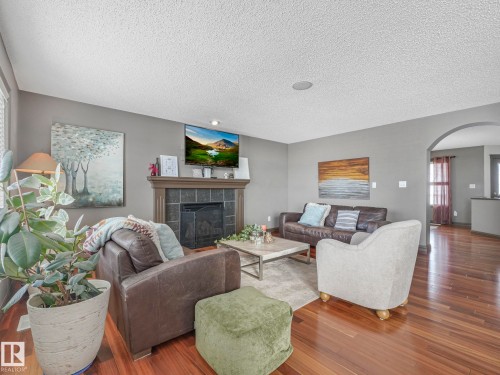 Living room with a tiled fireplace, arched walkways, wood finished floors, and a textured ceiling - 960 Summerside Link, Edmonton, AB - Indoor Photo Showing Living Room With Fireplace