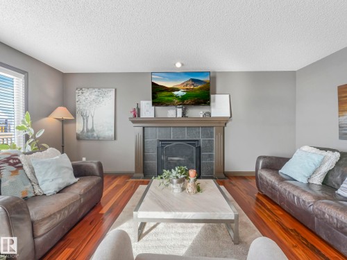 Living room with a fireplace, wood finished floors, and a textured ceiling - 960 Summerside Link, Edmonton, AB - Indoor Photo Showing Living Room With Fireplace