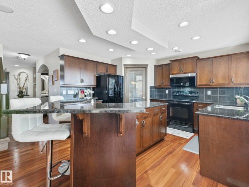 Kitchen featuring a textured ceiling, a breakfast bar, black appliances, decorative backsplash, and light wood-type flooring - 960 Summerside Link, Edmonton, AB - Indoor Photo Showing Kitchen