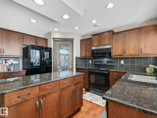 Kitchen with black appliances, dark stone countertops, tasteful backsplash, light wood-style flooring, and a textured ceiling - 960 Summerside Link, Edmonton, AB - Indoor Photo Showing Kitchen