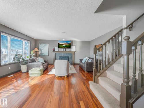Living area featuring wood-type flooring, a tile fireplace, and a textured ceiling - 960 Summerside Link, Edmonton, AB - Indoor Photo Showing Living Room With Fireplace