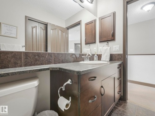 Half bathroom featuring a textured ceiling, vanity, tile walls, and wainscoting - 960 Summerside Link, Edmonton, AB - Indoor Photo Showing Bathroom