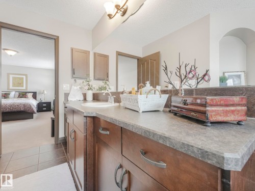 Ensuite bathroom with vanity, a textured ceiling, dark carpet, hanging lights, and dark tile patterned floors - 960 Summerside Link, Edmonton, AB - Indoor Photo Showing Bathroom