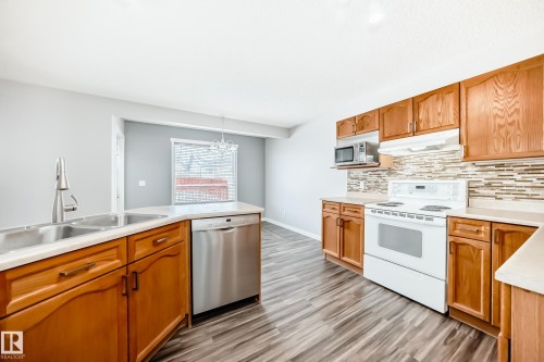 Kitchen featuring stainless steel appliances, light countertops, decorative backsplash, light wood finished floors, and hanging lights - 3208 29 Avenue, Edmonton, AB - Indoor Photo Showing Kitchen With Double Sink