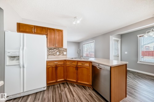 Kitchen with white refrigerator with ice dispenser, a peninsula, light countertops, dishwasher, and dark wood-type flooring - 3208 29 Avenue, Edmonton, AB - Indoor Photo Showing Kitchen With Double Sink