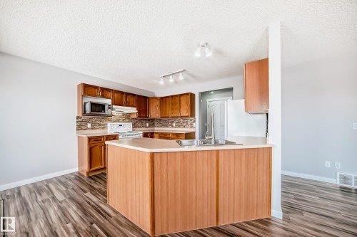 Kitchen with a peninsula, light countertops, dark wood-style floors, electric range, and a textured ceiling - 3208 29 Avenue, Edmonton, AB - Indoor Photo Showing Kitchen With Double Sink