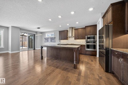 Kitchen with light stone counters, dark wood finish cabinets, an island with sink, stainless steel appliances, and a textured ceiling - 1907 Adamson Terrace, Edmonton, AB - Indoor Photo Showing Kitchen With Upgraded Kitchen