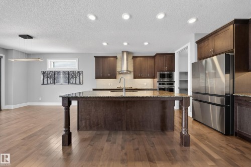 Kitchen with dark wood finish cabinetry, light stone counters, stainless steel appliances, a kitchen breakfast bar, and a center island with sink - 1907 Adamson Terrace, Edmonton, AB - Indoor Photo Showing Kitchen