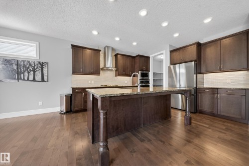 Kitchen with an island with sink, stainless steel appliances, dark wood-style floors, light stone countertops, and dark wood finish cabinetry - 1907 Adamson Terrace, Edmonton, AB - Indoor Photo Showing Kitchen With Upgraded Kitchen