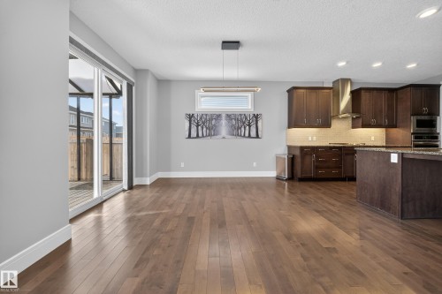 Kitchen featuring dark wood finish cabinetry, dark wood-style flooring, light stone counters, stainless steel appliances, and decorative light fixtures - 1907 Adamson Terrace, Edmonton, AB - Indoor Photo Showing Kitchen