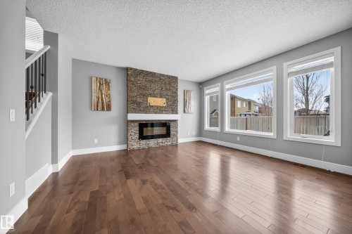 Unfurnished living room with a stone fireplace, a textured ceiling, and dark wood-type flooring - 1907 Adamson Terrace, Edmonton, AB - Indoor Photo Showing Living Room With Fireplace