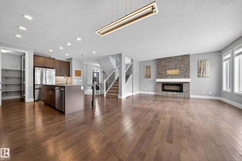 Kitchen featuring open floor plan, a kitchen island with sink, stainless steel appliances, a textured ceiling, and a stone fireplace - 1907 Adamson Terrace, Edmonton, AB - Indoor