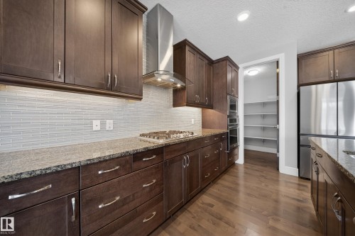 Kitchen with dark wood finish cabinetry, light stone counters, dark wood-style floors, stainless steel appliances, and a textured ceiling - 1907 Adamson Terrace, Edmonton, AB - Indoor Photo Showing Kitchen With Upgraded Kitchen