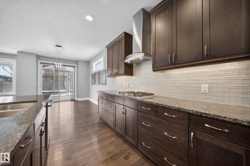 Kitchen with dark stone countertops, dark wood finish cabinetry, dark wood-type flooring, pendant lighting, and tasteful backsplash - 1907 Adamson Terrace, Edmonton, AB - Indoor Photo Showing Kitchen With Upgraded Kitchen