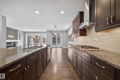Kitchen with dark wood finish cabinetry, dark stone countertops, a fireplace, dark wood-style flooring, and a textured ceiling - 1907 Adamson Terrace, Edmonton, AB - Indoor Photo Showing Kitchen With Double Sink With Upgraded Kitchen