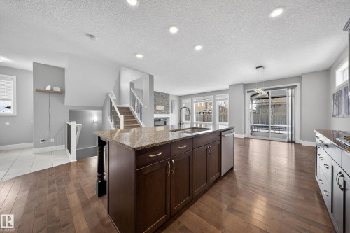 Kitchen featuring a center island with sink, light stone counters, dark wood finish cabinetry, dark wood-type flooring, and a textured ceiling - 1907 Adamson Terrace, Edmonton, AB - Indoor Photo Showing Kitchen With Upgraded Kitchen