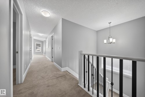 Hallway featuring light carpet, a textured ceiling, suspended lighting, and an upstairs landing - 1907 Adamson Terrace, Edmonton, AB - Indoor Photo Showing Other Room