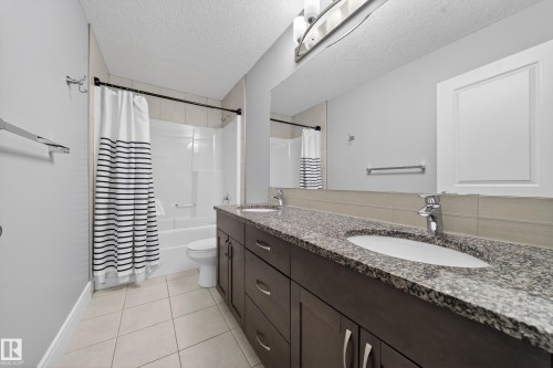Full bathroom featuring double vanity, shower / bath combo with shower curtain, a textured ceiling, and light tile patterned floors - 1907 Adamson Terrace, Edmonton, AB - Indoor Photo Showing Bathroom