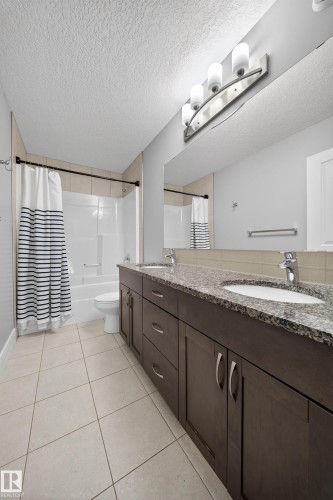 Full bath featuring double vanity, shower / bath combo, a textured ceiling, and light tile patterned floors - 1907 Adamson Terrace, Edmonton, AB - Indoor Photo Showing Bathroom