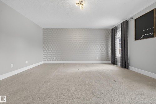 Spare room featuring light colored carpet, wallpapered walls, an accent wall, and a textured ceiling - 1907 Adamson Terrace, Edmonton, AB - Indoor Photo Showing Other Room