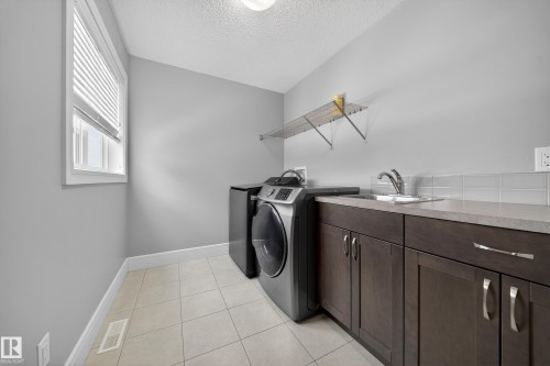 Laundry area with light tile patterned floors, a textured ceiling, cabinet space, and washer and clothes dryer - 1907 Adamson Terrace, Edmonton, AB - Indoor Photo Showing Laundry Room