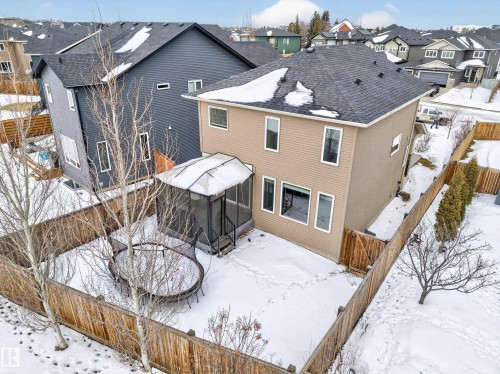 Snow covered house featuring a fenced backyard, a residential view, a sunroom, a shingled roof, and a trampoline - 1907 Adamson Terrace, Edmonton, AB - Outdoor