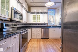 Kitchen with stainless steel appliances, glass insert cabinets, light wood-style flooring, track lighting, and dark stone countertops - 