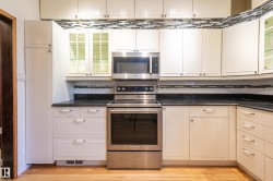 Kitchen featuring glass insert cabinets, appliances with stainless steel finishes, cream cabinetry, decorative backsplash, and dark stone counters - 
