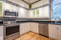 Kitchen featuring glass insert cabinets, stainless steel appliances, light wood finished floors, cream cabinets, and dark stone counters - 