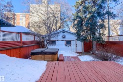 Snow covered deck with a hot tub, a fenced backyard, and an outbuilding - 