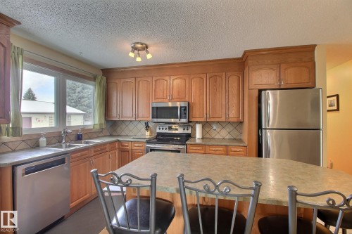 Kitchen with a kitchen breakfast bar, stainless steel appliances, wood finish cabinets, tasteful backsplash, and a textured ceiling - 4520 20A Avenue, Edmonton, AB - Indoor Photo Showing Kitchen With Double Sink
