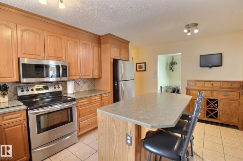Kitchen featuring stainless steel appliances, a center island, light tile patterned floors, decorative backsplash, and a kitchen bar - 4520 20A Avenue, Edmonton, AB - Indoor Photo Showing Kitchen
