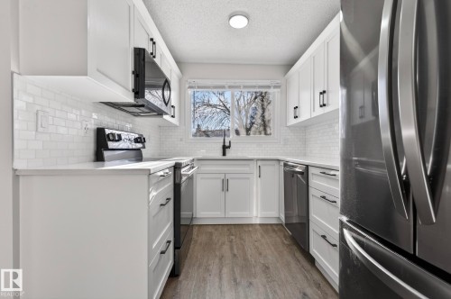 Kitchen with stainless steel appliances, white cabinetry, dark wood finished floors, a textured ceiling, and light stone counters - 9969 171 Avenue, Edmonton, AB - Indoor Photo Showing Kitchen With Stainless Steel Kitchen