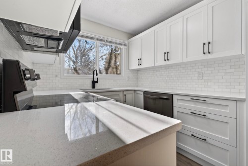 Kitchen with white cabinetry, range hood, light stone counters, backsplash, and a textured ceiling - 9969 171 Avenue, Edmonton, AB - Indoor Photo Showing Kitchen