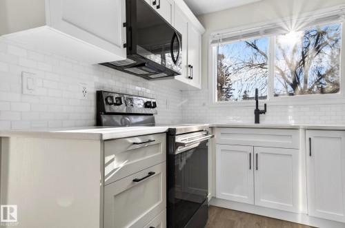 Kitchen featuring black electric range oven, white cabinets, light stone countertops, dark wood-style floors, and backsplash - 9969 171 Avenue, Edmonton, AB - Indoor Photo Showing Kitchen